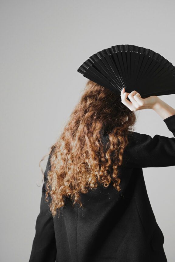 long curly haired figure with a black fan held above her head